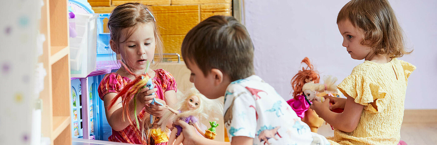 Zwei Mädchen und ein Bube sitzen am Boden und spiele mit Barbies