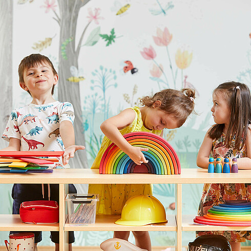 Drei Kinder im Vorschulalter spielen konzentriert mit bunten Holzspielzeug