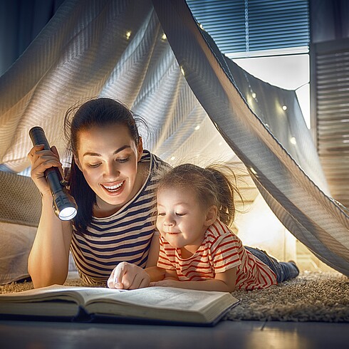 Mutter liest Tochter mit einer Taschenlampe aus einem Buch vor