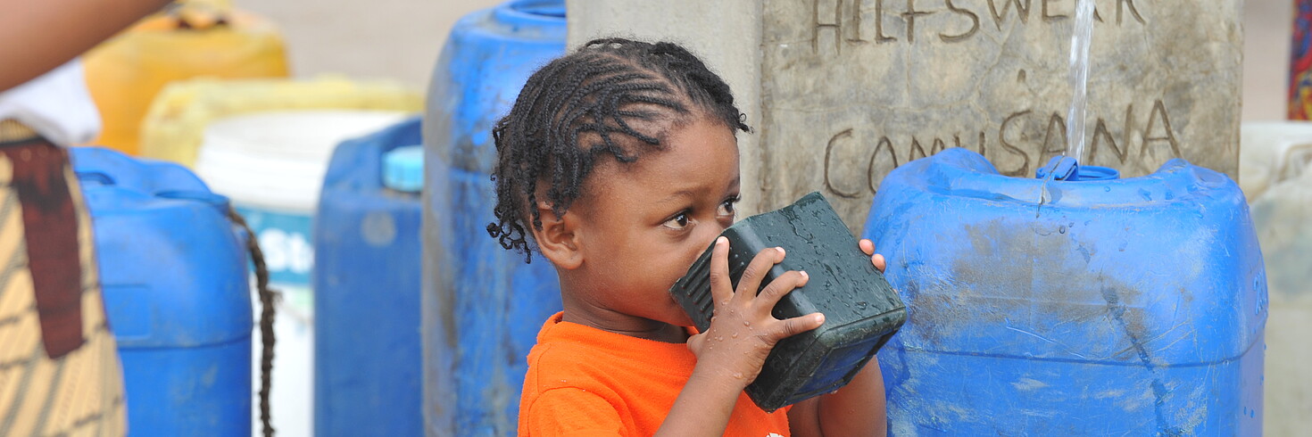 Kind in Mosambik trinkt Wasser vor Hilfswerk Brunnen