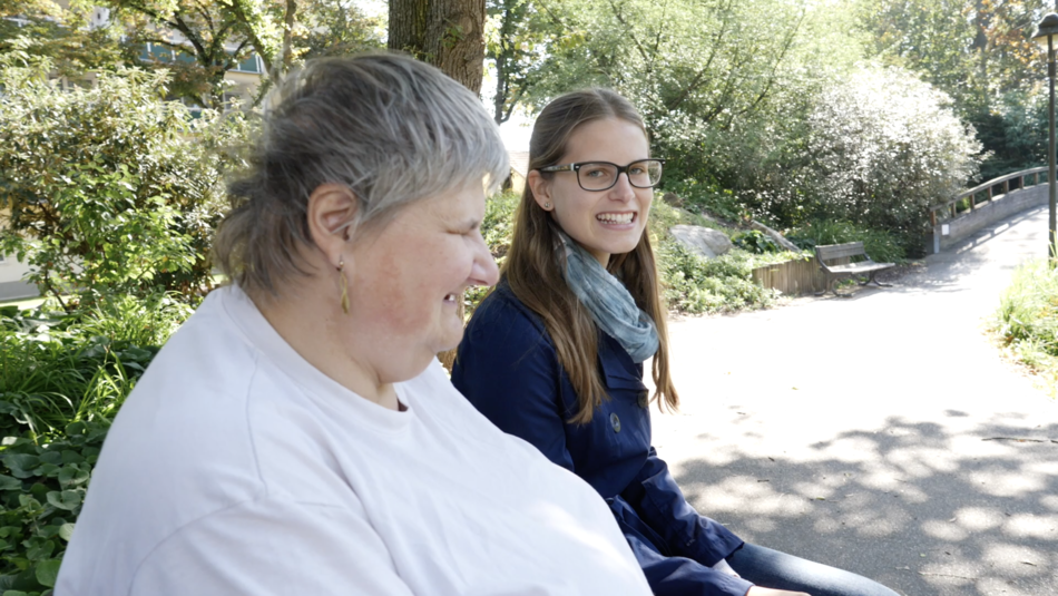 ehrenamtliche Besucherin beim Plaudern mit einer Besuchten auf einer Bank im Park