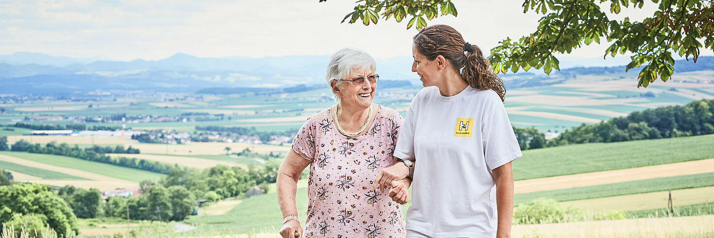 Hilfswerkerin spaziert gemeinsam mit einer älteren Dame in der Natur