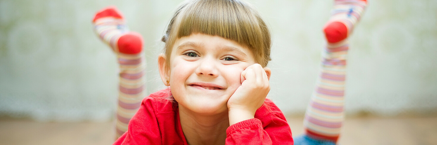 Copyright: Fotolia Auf dem Bauch liegendes Mädchen lächelt in Kamera