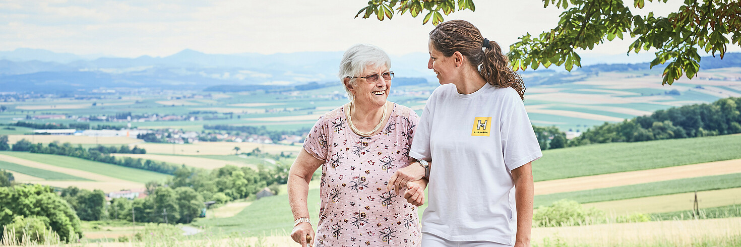 Hilfswerkerin spaziert gemeinsam mit einer älteren Dame in der Natur