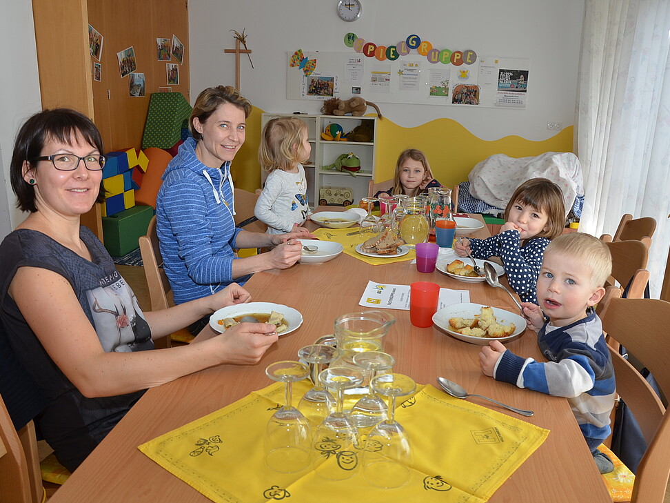 vier kleine Kinder und zwei Betreuerinnen sitzen am Tisch und essen