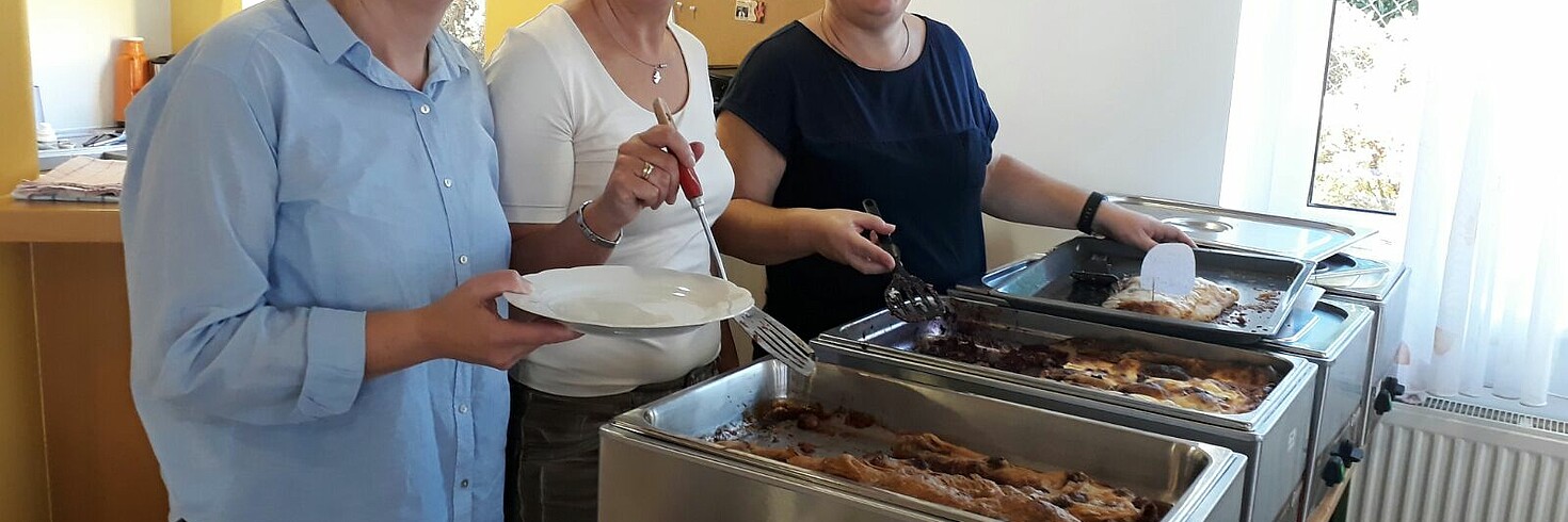 3 Frauen stehen am Herd und geben Essen aus