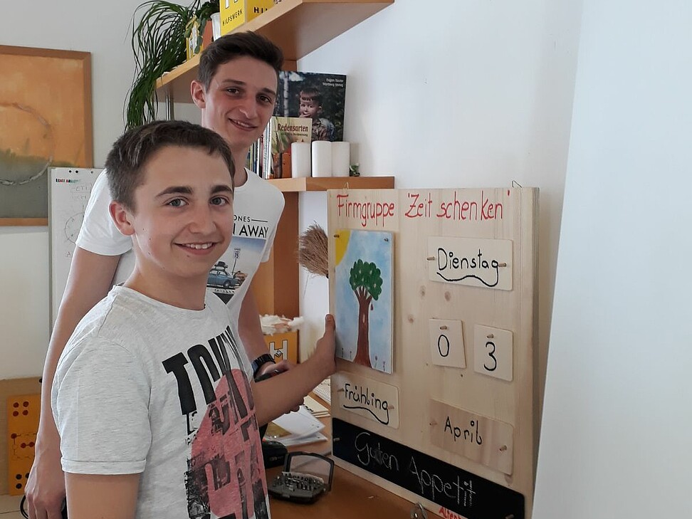 2 junge Burschen stehen vor dem mitgebrachten Geschenk, einem Kalender