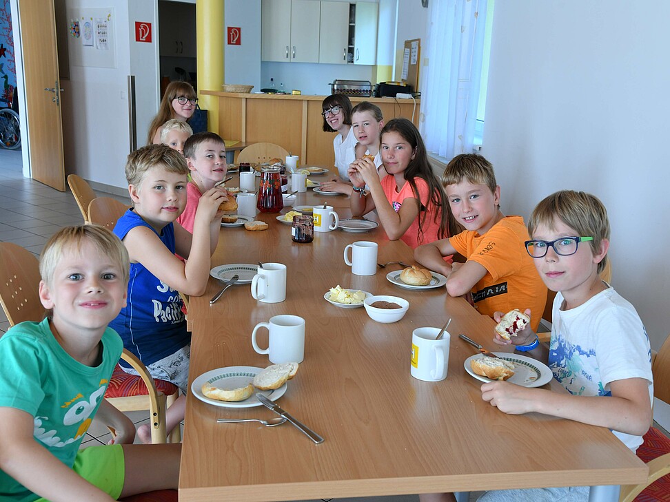10 Kinder sitzen am Tisch und geniesen das gemeinsame Frühstück