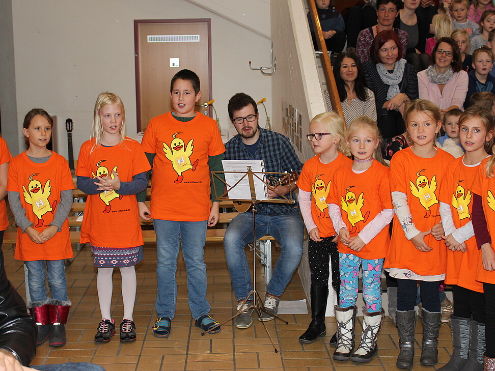 Kinder werden von Gitarrenklängen beim Singen begleitet