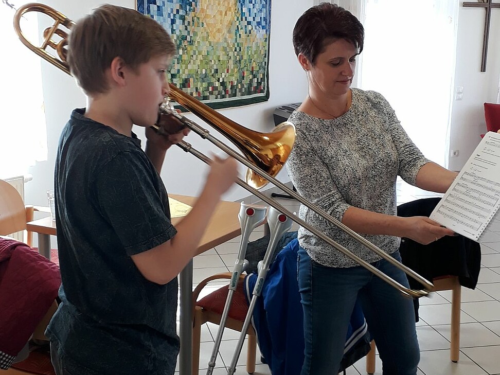 ein Jugendlicher spielt Trompete und die Lehrerin hält die Noten bereit