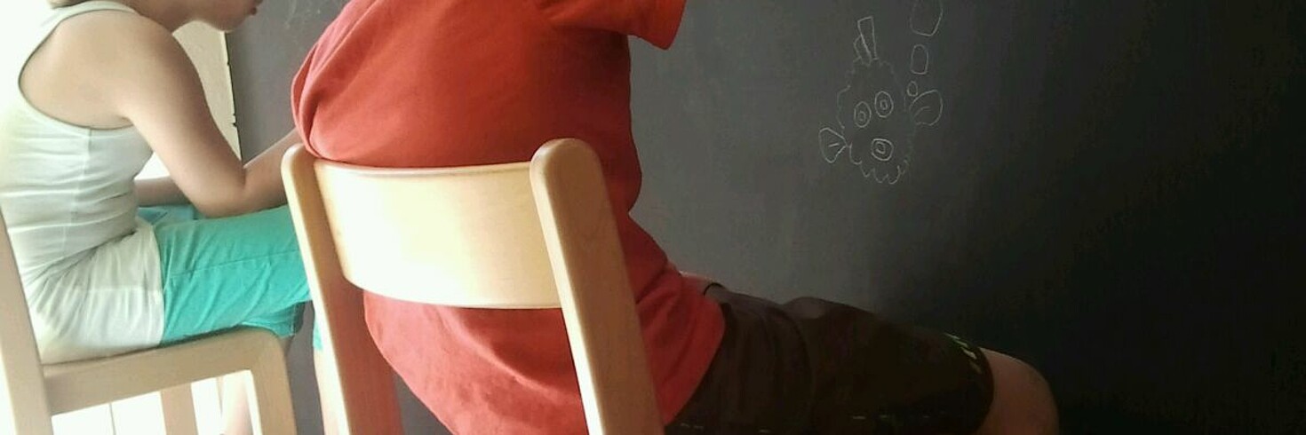 Mädchen und Jungen sitzten zeichnend an einer großen Tafel