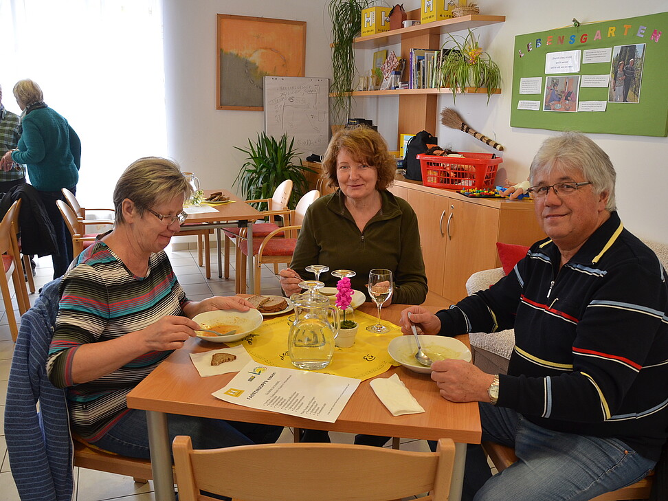 zwei Frauen und ein Mann sitzen am Tisch und essen Suppe