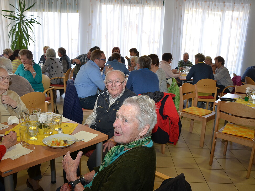 viele alte Leute sitzen an Tischen und essen Fastensuppe