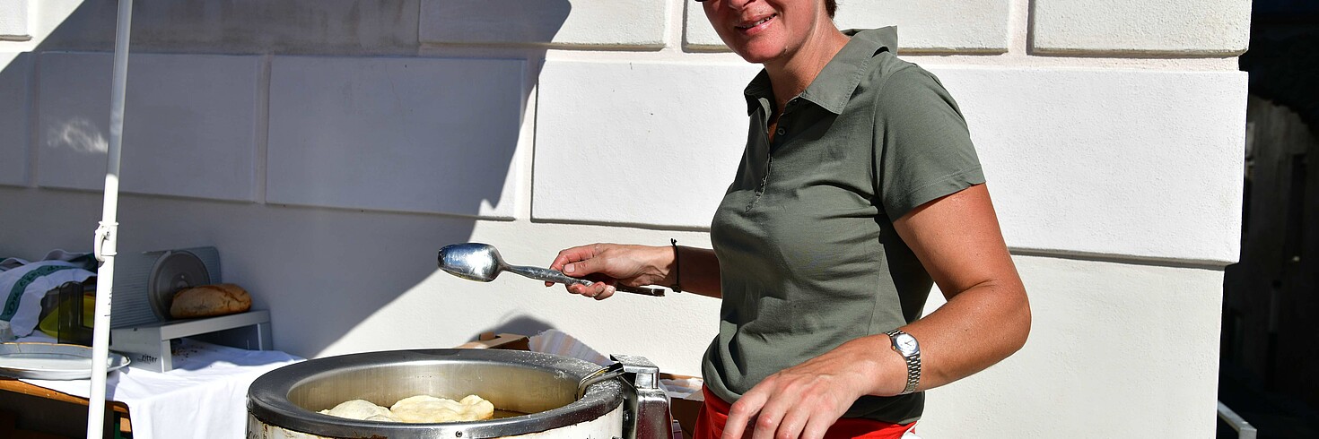 eine Frau steht unter einem Sonnenschirm und bäckt Krapfen