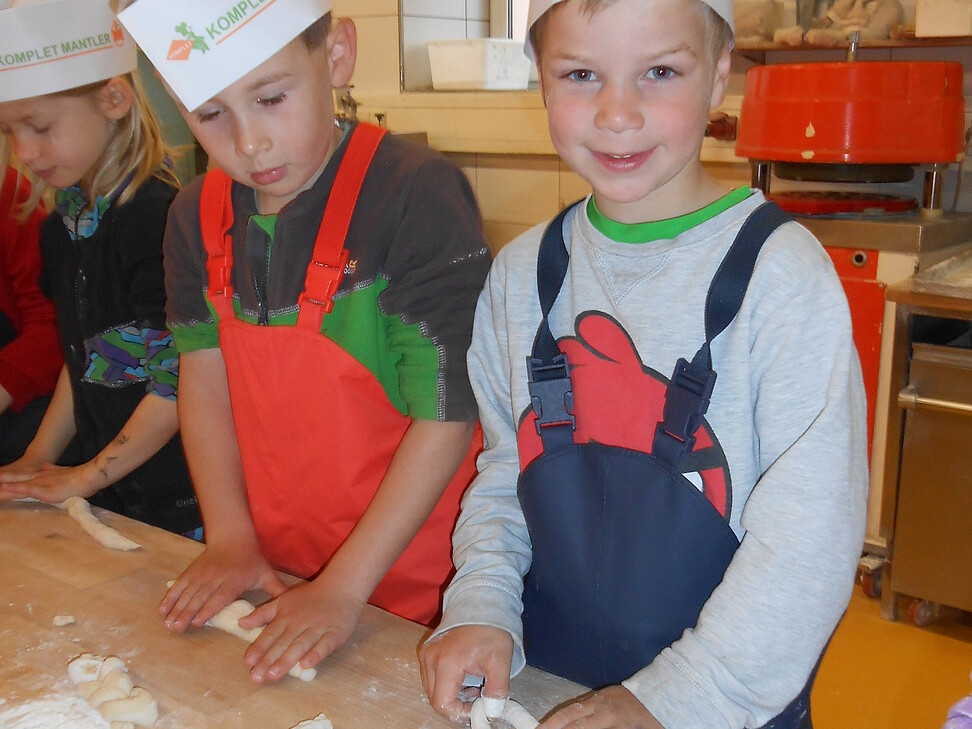 3 Kinder mit Kopfbedeckung beim Teigrollen