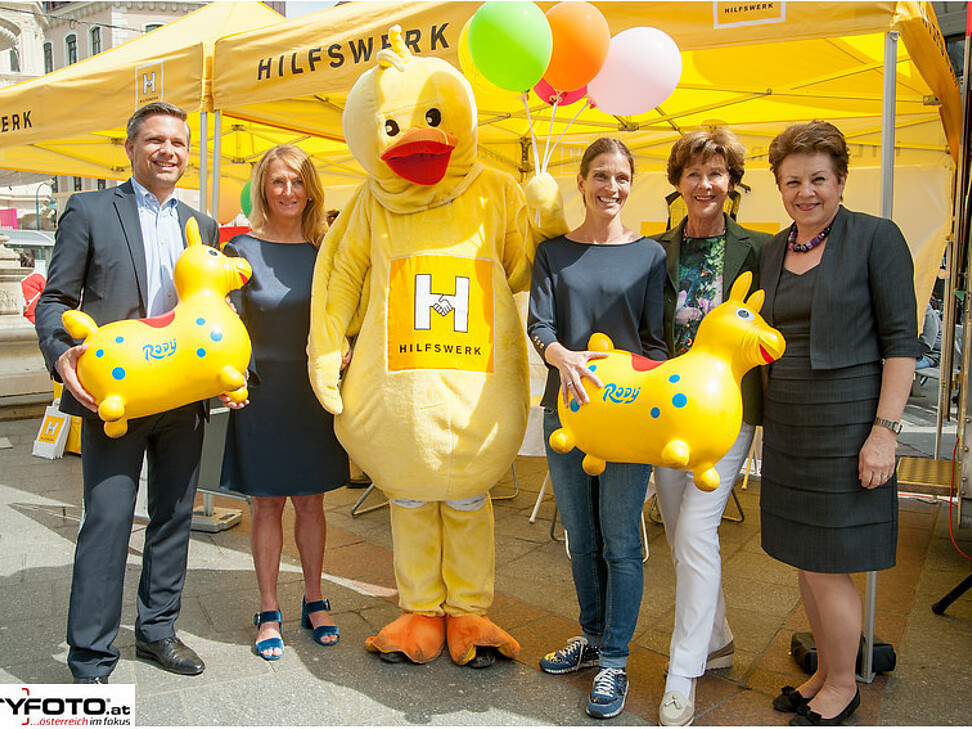 5 Personen und das Moskottchen posieren für ein Gruppenfoto