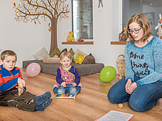 Eine Gruppe Kinder sitzt mit der Pädagogin in einem Kreis am Boden