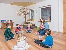 Eine Gruppe Kinder sitzt mit der Pädagogin in einem Kreis am Boden