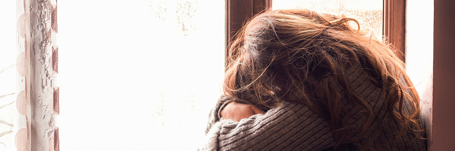 Frau in Angsthaltung vor Fenster