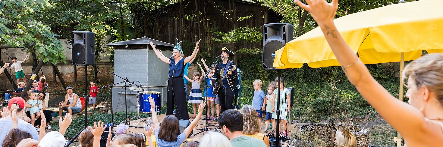 Zwei Personen Performen mit Kindern auf der Bühne vor einem Publikum.
