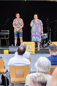 Eine Frau und ein Mann stehen vor einem Publikum auf der Bühne.