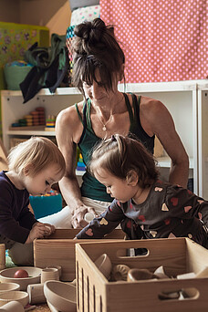 Eine Tagesmutter spielt mit zwei Kleinkindern.