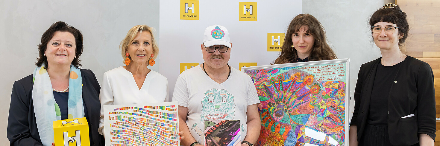 Fünf Personen stehen nebeneinander und halten die Gewinner-Kunstwerke, während sie in die Kamera lächeln