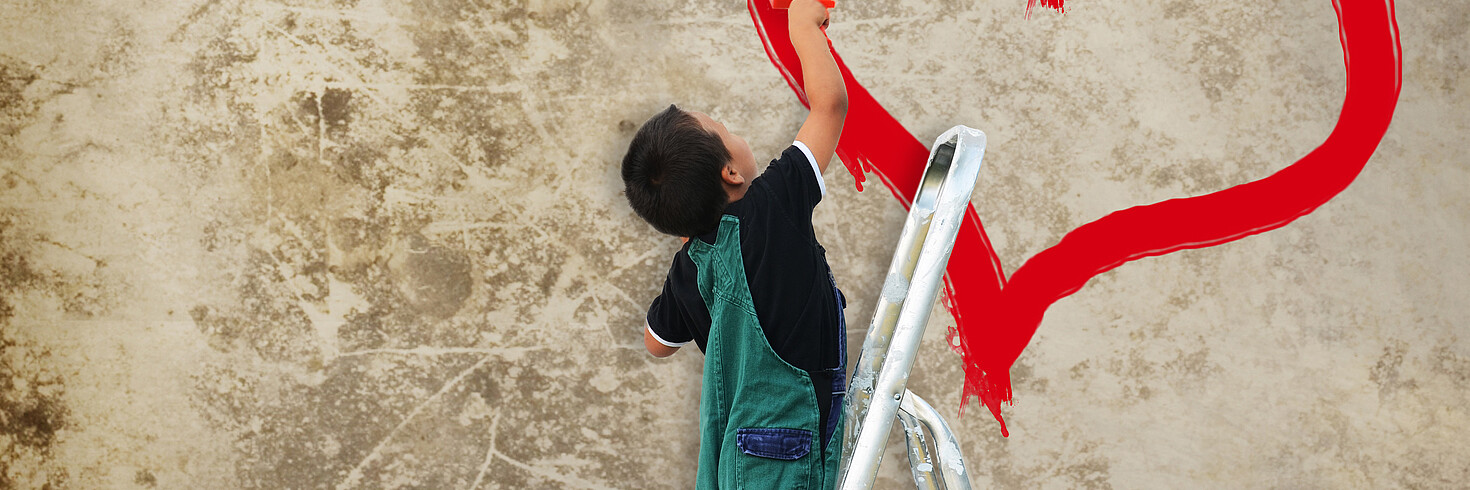 Kind malt rotes Herz auf grau-braune Wand