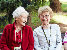 Zwei Frauen sitzen auf eine Parkbank und lächeln