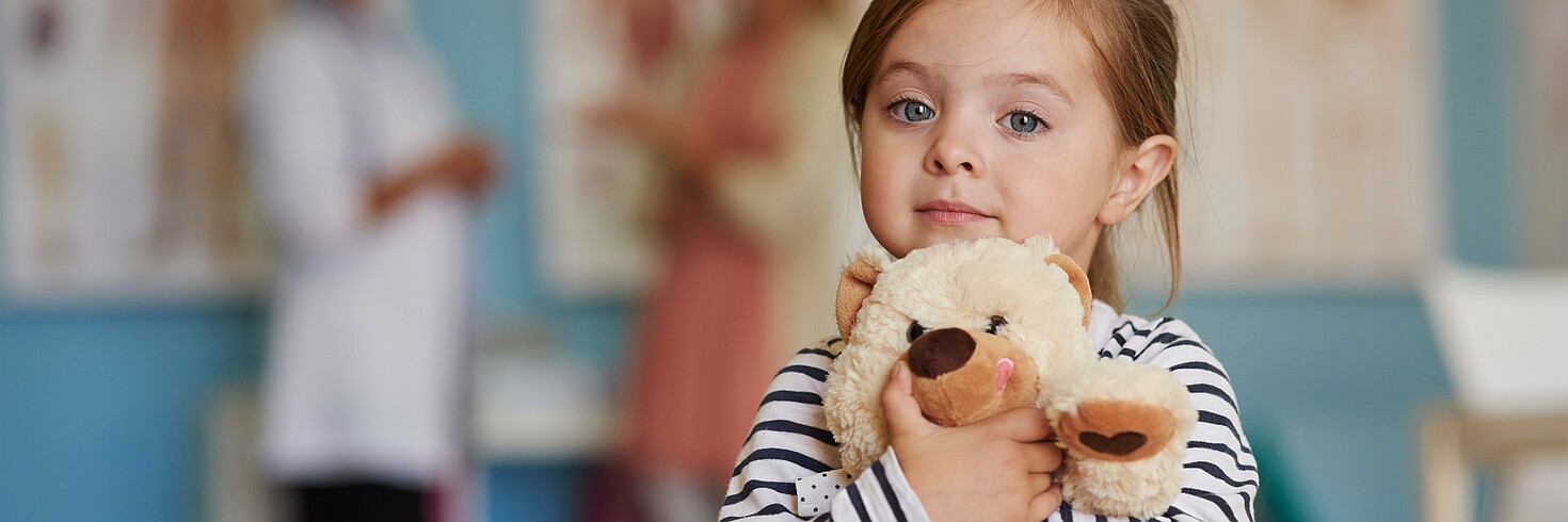 kleines Mädchen hält Teddybär und sieht hoffnungsvoll in die Kamera