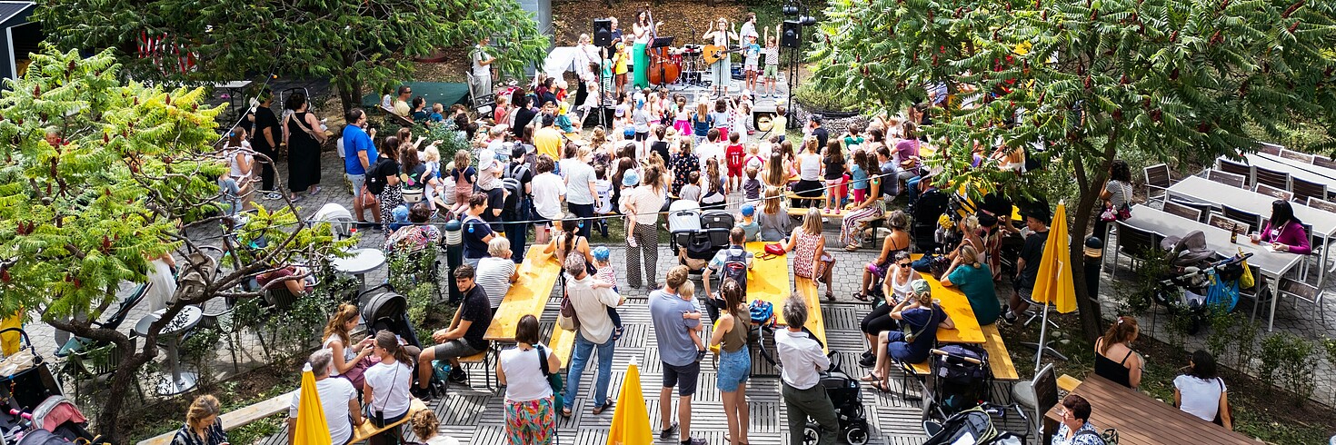 Viele Menschen stehen im Garten und sehen einer Live-Band auf der Bühne zu.