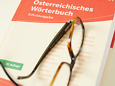 Bild von einem österreichischen Wörterbuch. Eine Brille liegt auf dem Buch.