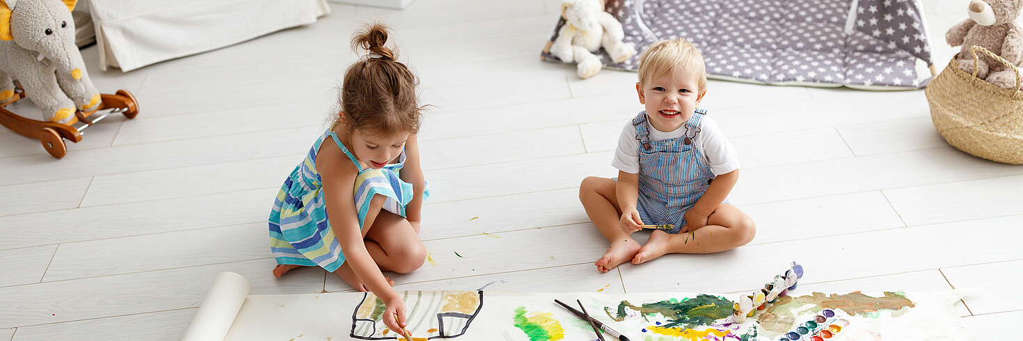 zwei Kleinkinder sitzen am Boden und malen