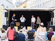 Vier Personen stehen vor einem Publikum auf der Bühne.