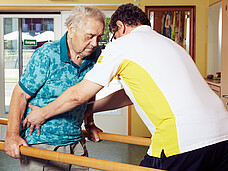 Physiotherapeut unterstützt älteren Mann beim Gehen