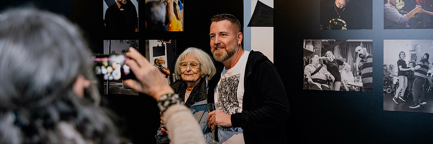 Zwei Menschen posieren auf einer Fotoausstellung vor den Ausstellungsstücken..