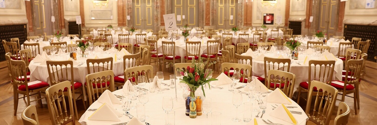 Eingedeckte Tische in einem Festsaal.