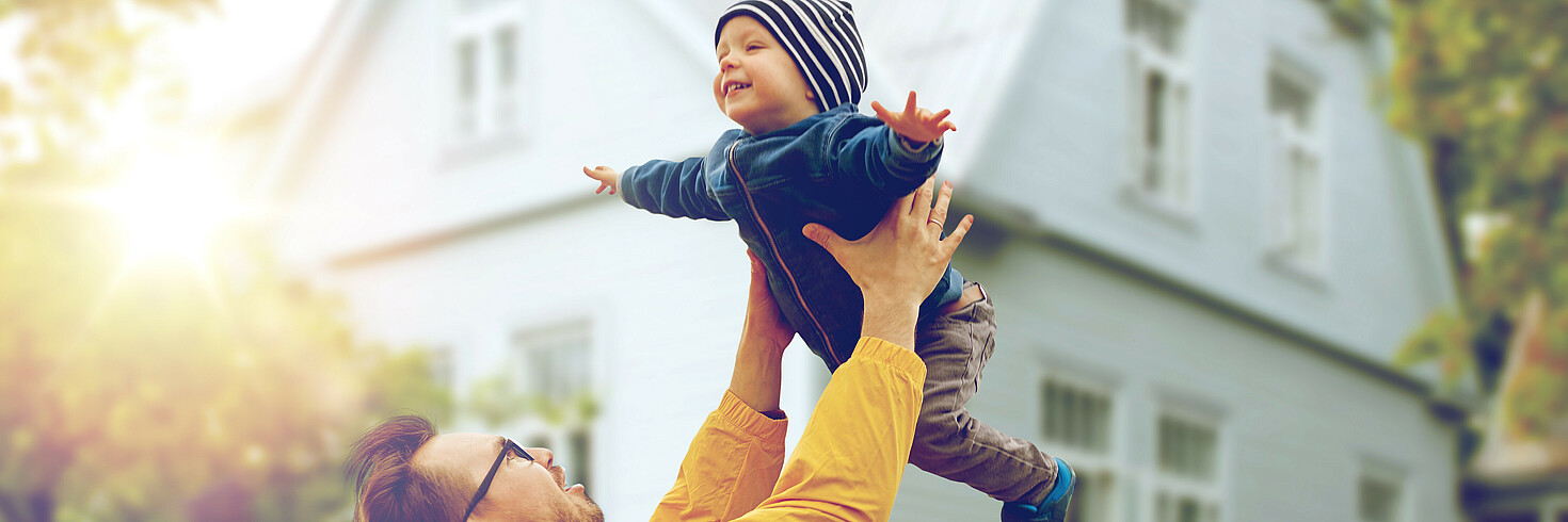 Ein Mann wirft ein Kleinkind hoch. Beide lachen.