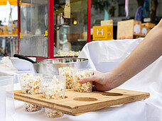 Eine Hand greift nach einem Becher Popcorn.