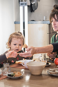 Eine Tagesmutter sitzt mit zwei Kleinkindern am Tisch beim Frühstück.