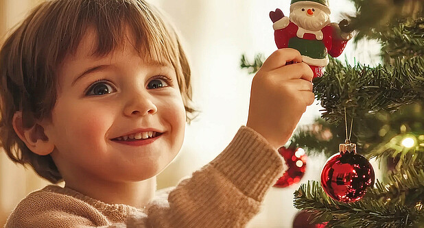 Kleines Kind steht vor einem festlich geschmückten Weihnachtsbaum