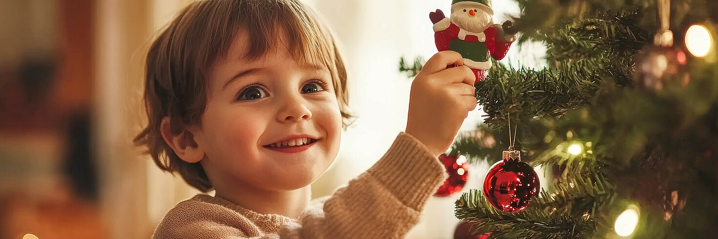 Kleines Kind steht vor einem festlich geschmückten Weihnachtsbaum