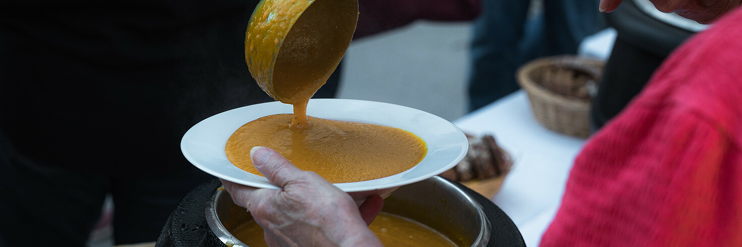 Mit einem Schöpfer wird Suppe in einen Suppenteller gegossen