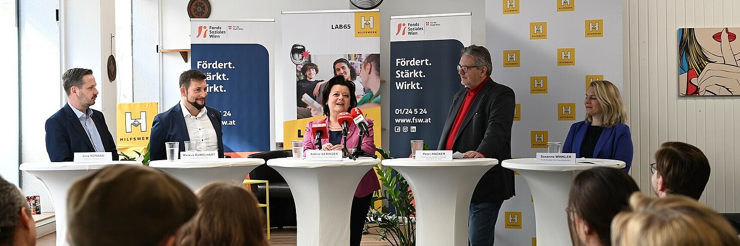 Fünf Personen stehen auf einer Bühne uns sprechen vor Publikum.